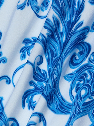 Introducing the Nicole Bikini Bottom, featuring white fabric adorned with an intricate blue baroque print of floral and swirl motifs. Slightly folded to reveal texture and detail, this piece is crafted from four-way stretch nylon for moderate coverage.