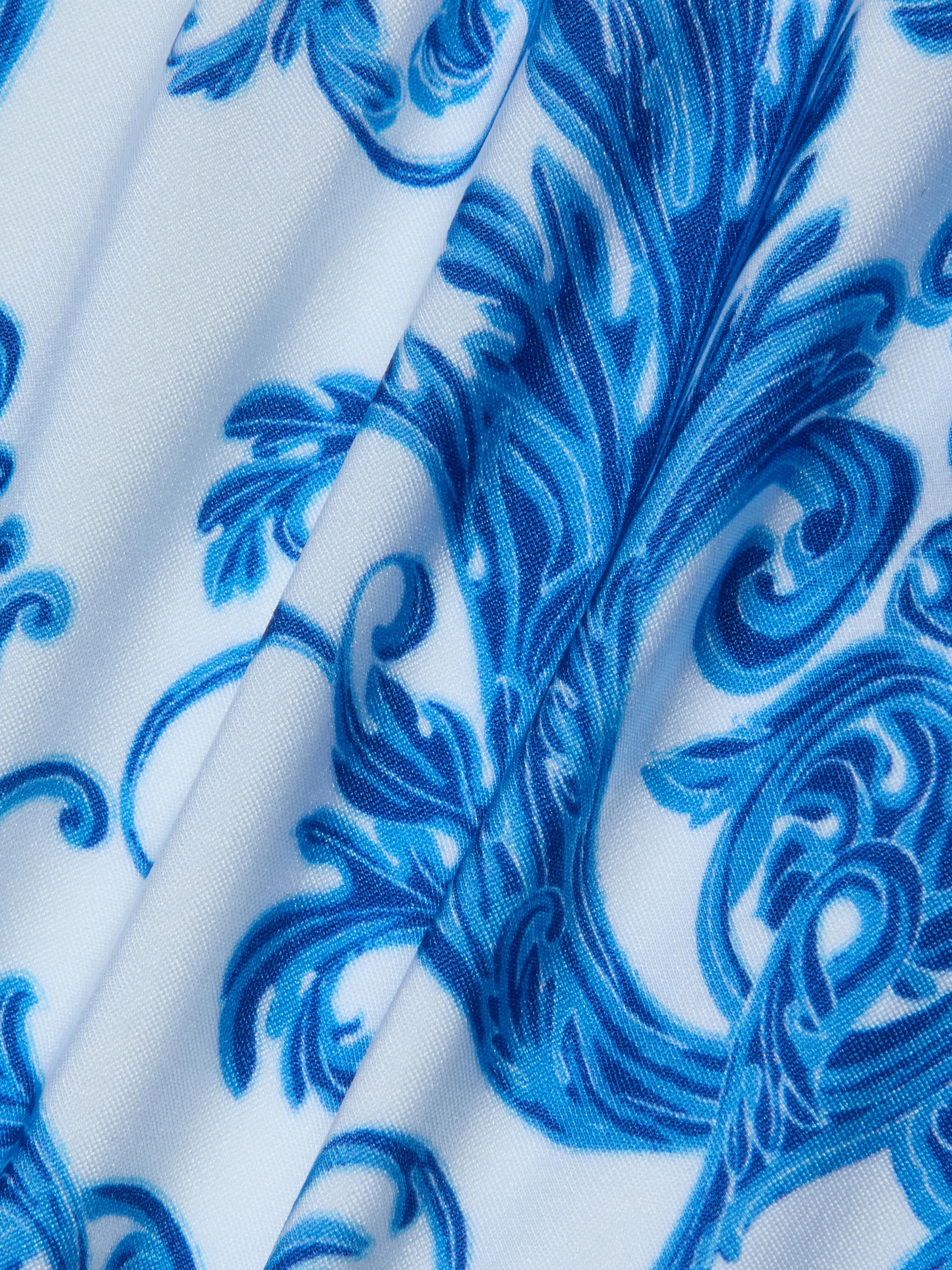 Introducing the Nicole Bikini Bottom, featuring white fabric adorned with an intricate blue baroque print of floral and swirl motifs. Slightly folded to reveal texture and detail, this piece is crafted from four-way stretch nylon for moderate coverage.