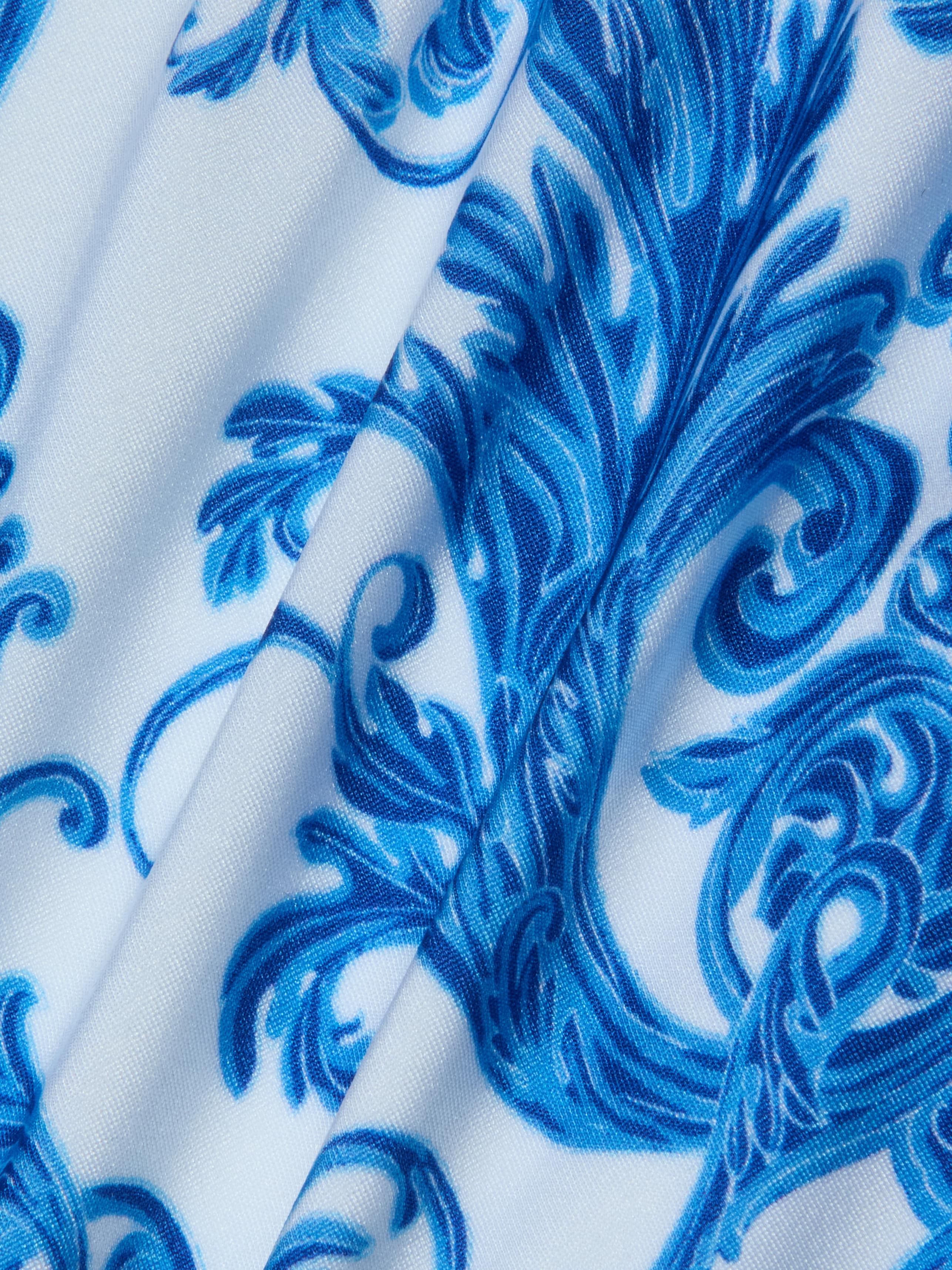 Introducing the Nicole Bikini Bottom, featuring white fabric adorned with an intricate blue baroque print of floral and swirl motifs. Slightly folded to reveal texture and detail, this piece is crafted from four-way stretch nylon for moderate coverage.