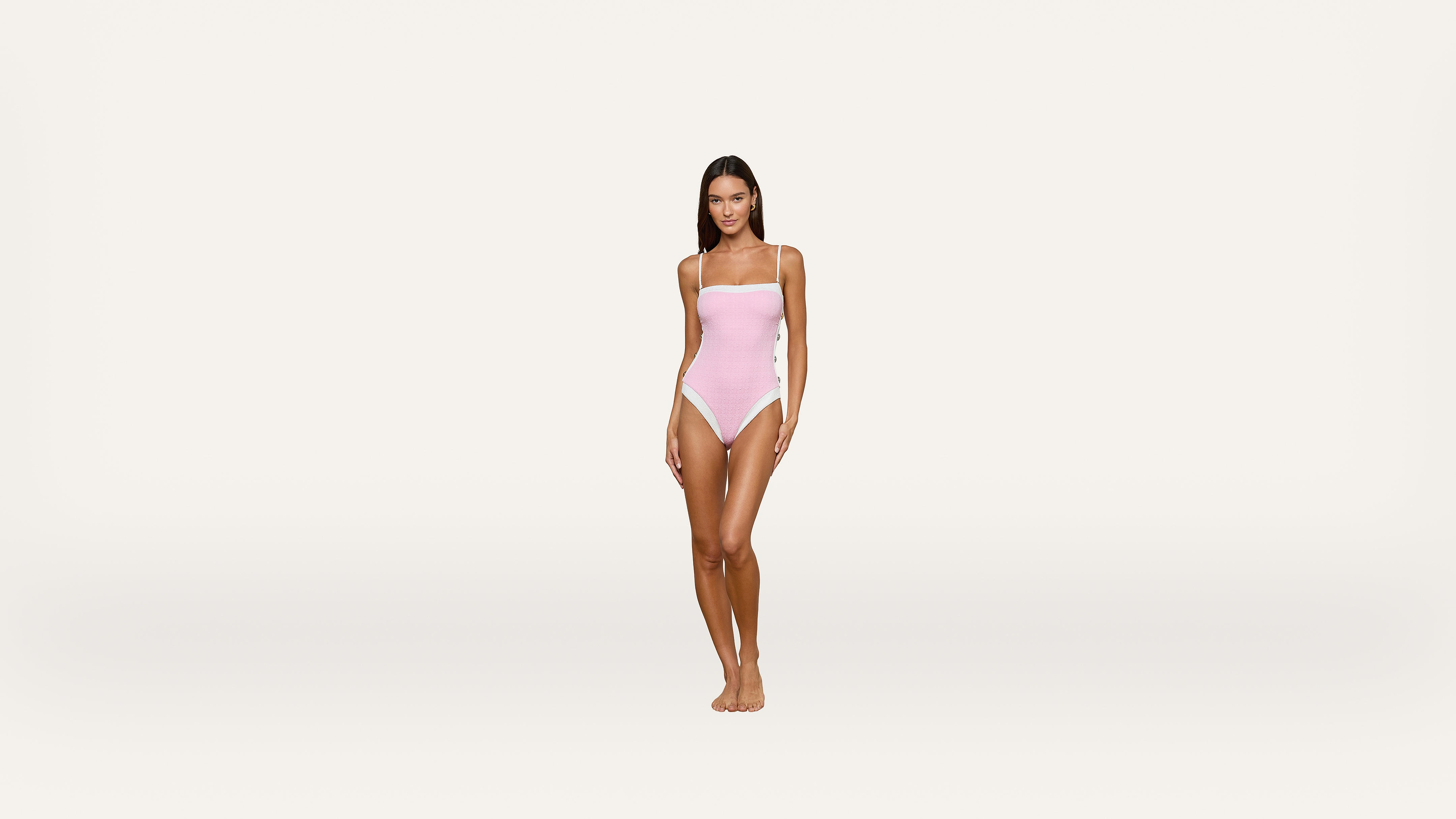 A woman stands facing forward, wearing a light pink one-piece swimsuit against a plain white background.