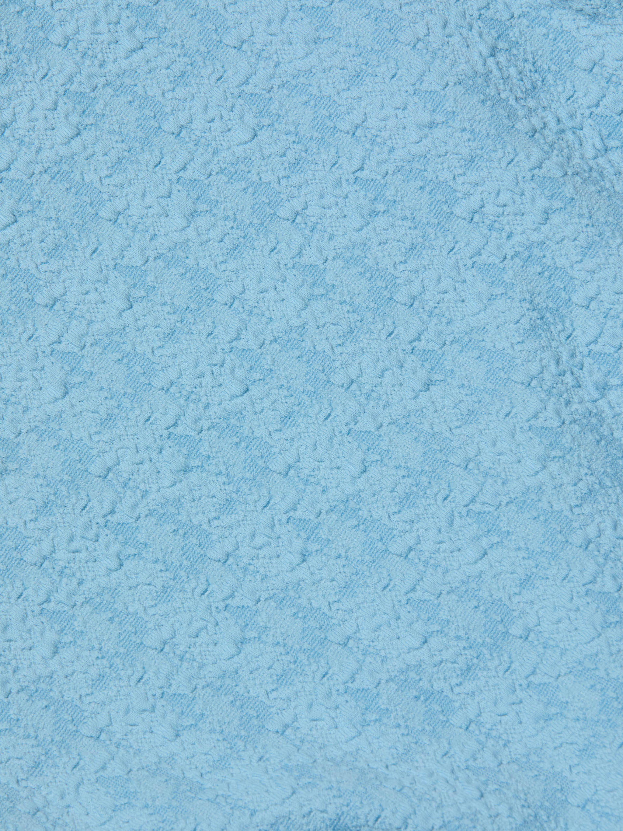 Close-up of the Tory Bandeau One-Piece Swimsuit in light blue bouclé fabric, featuring a subtle floral or geometric pattern woven throughout the material.