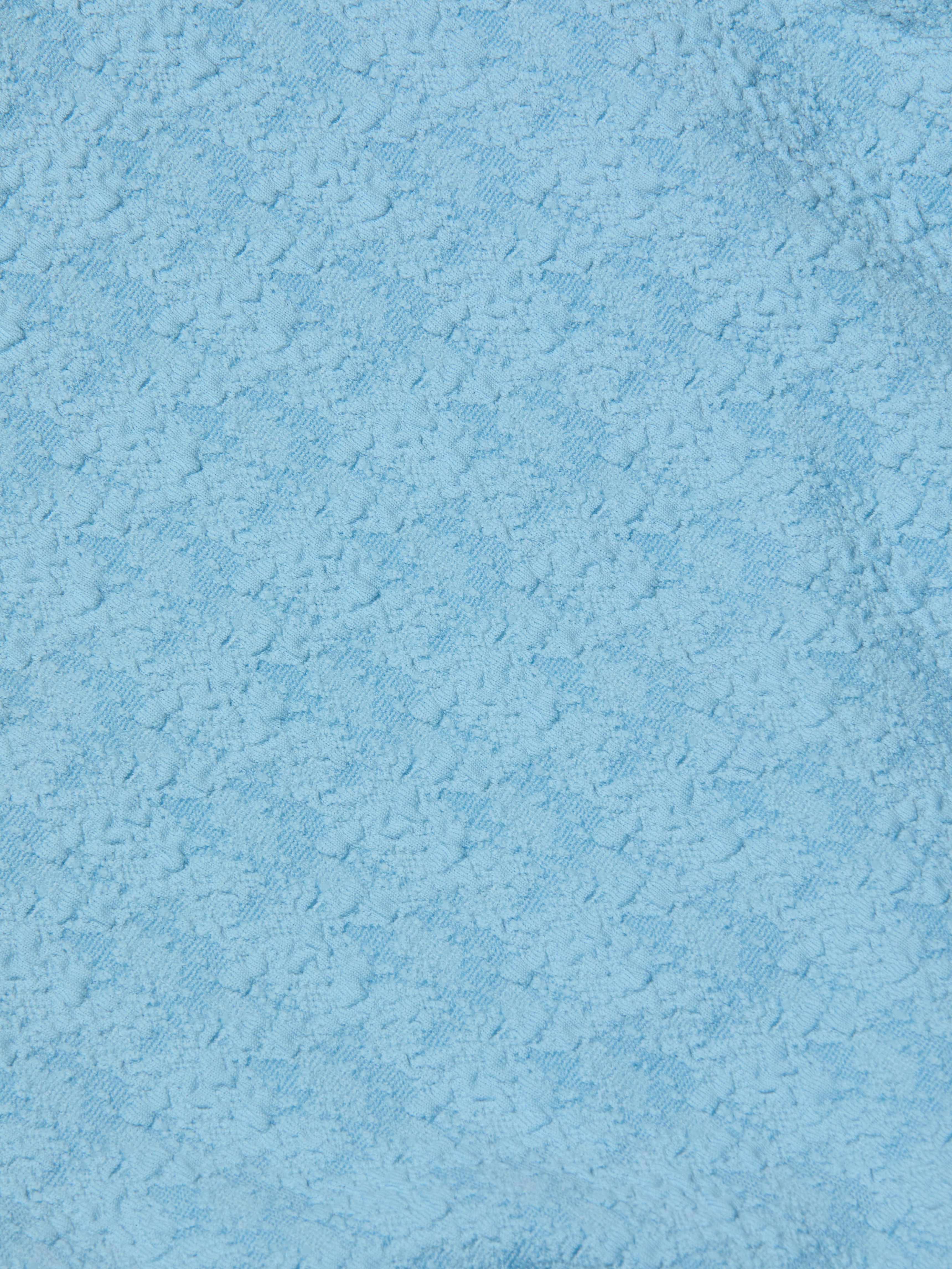 Close-up of the Tory Bandeau One-Piece Swimsuit in light blue bouclé fabric, featuring a subtle floral or geometric pattern woven throughout the material.