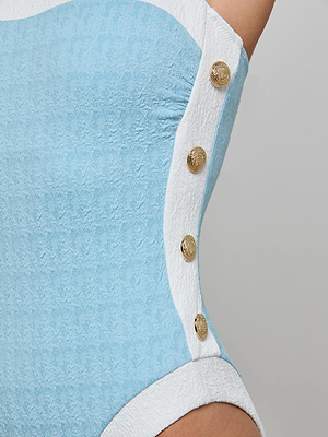 Close-up of the Tory Bandeau One-Piece Swimsuit in powder blue and white bouclé, featuring gold decorative buttons on the white side panel, shown on the hip and waist against a plain background.