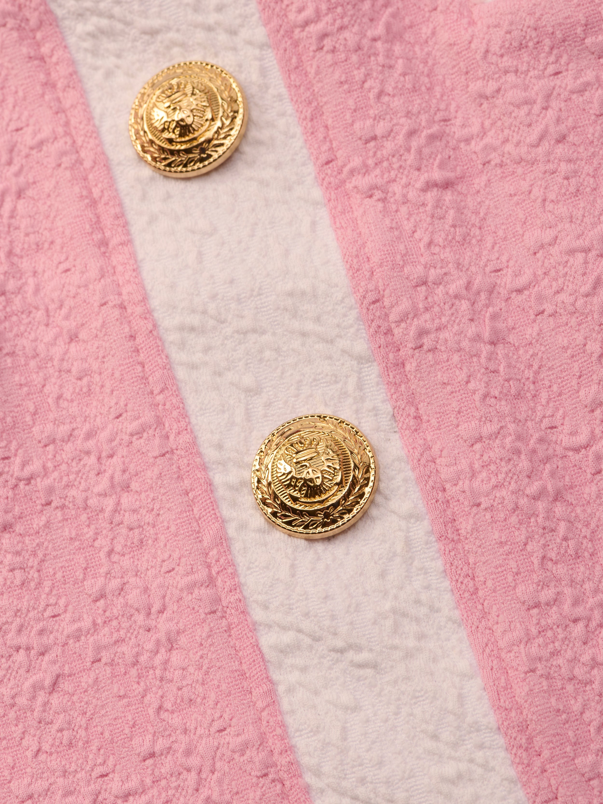 Close-up of the Coco Mini Skirt Cover-Up in pink bouclé fabric with two gold embossed buttons and a vertical off-white stripe—ideal as a chic swimsuit cover-up.