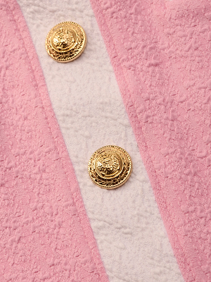 Close-up of the Coco Mini Skirt Cover-Up in pink bouclé fabric with two gold embossed buttons and a vertical off-white stripe—ideal as a chic swimsuit cover-up.