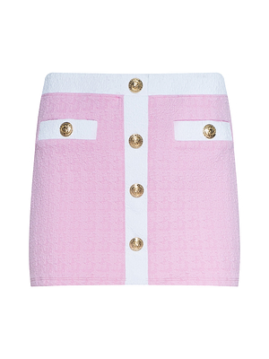 The Coco Mini Skirt Cover-Up is a pink textured bouclé mini skirt with white panels, six gold buttons in two rows, and two front buttoned pockets—ideal for adding chic style over your swimsuit.