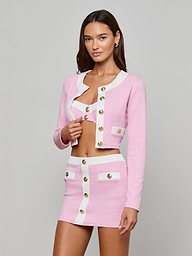A woman models the Adaline Cardigan Cover-Up, a stylish textured bouclé pink and white two-piece with gold buttons, including a cropped jacket, bralette, and high-waisted mini skirt with pockets against a plain light gray background.