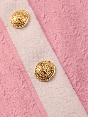 Close-up of two ornate gold buttons on textured pink bouclé fabric with a beige diagonal stripe—Adaline Cardigan Cover-Up is a chic, water-safe layer perfect for the beach or as a stylish cardigan.