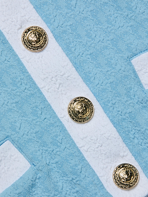 Close-up of the Adaline Cardigan Cover-Up in powder blue and white textured fabric, detailed with three gold emblem buttons, diagonal white stripes, and visible pocket edges—perfect for a chic beach cover-up.