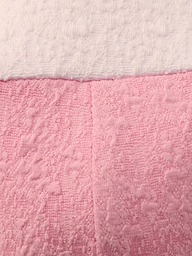 Close-up of the Alexandria Bikini Top’s textured bouclé fabric: white on top, pink on bottom, divided by a horizontal seam. The pink section is shaped like a balconette with underwire and has a vertical center seam.