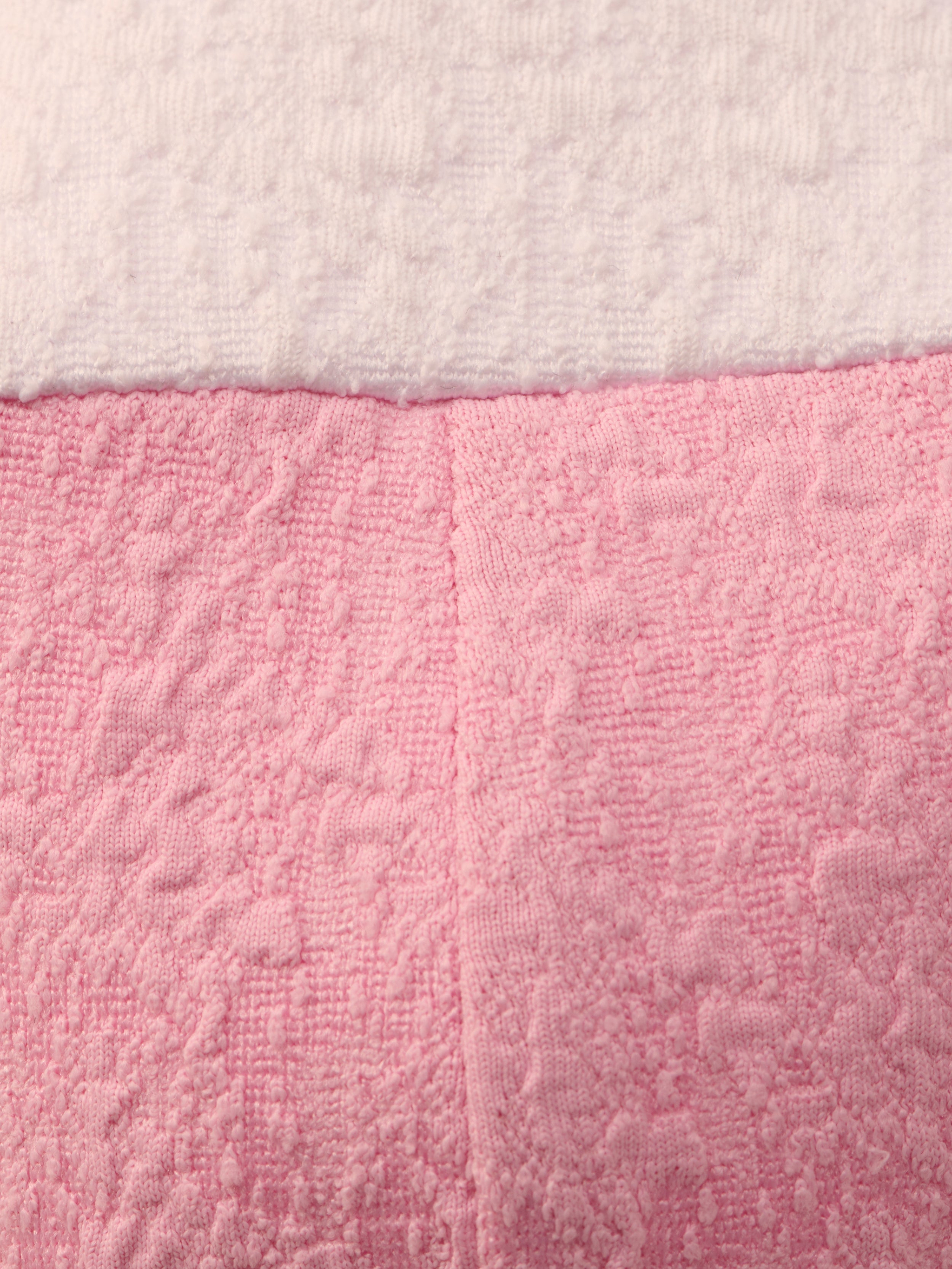 Close-up of the Alexandria Bikini Top’s textured bouclé fabric: white on top, pink on bottom, divided by a horizontal seam. The pink section is shaped like a balconette with underwire and has a vertical center seam.