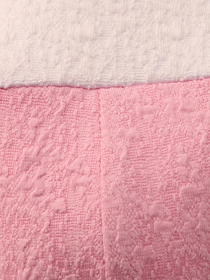 Close-up of the Alexandria Bikini Top’s textured bouclé fabric: white on top, pink on bottom, divided by a horizontal seam. The pink section is shaped like a balconette with underwire and has a vertical center seam.
