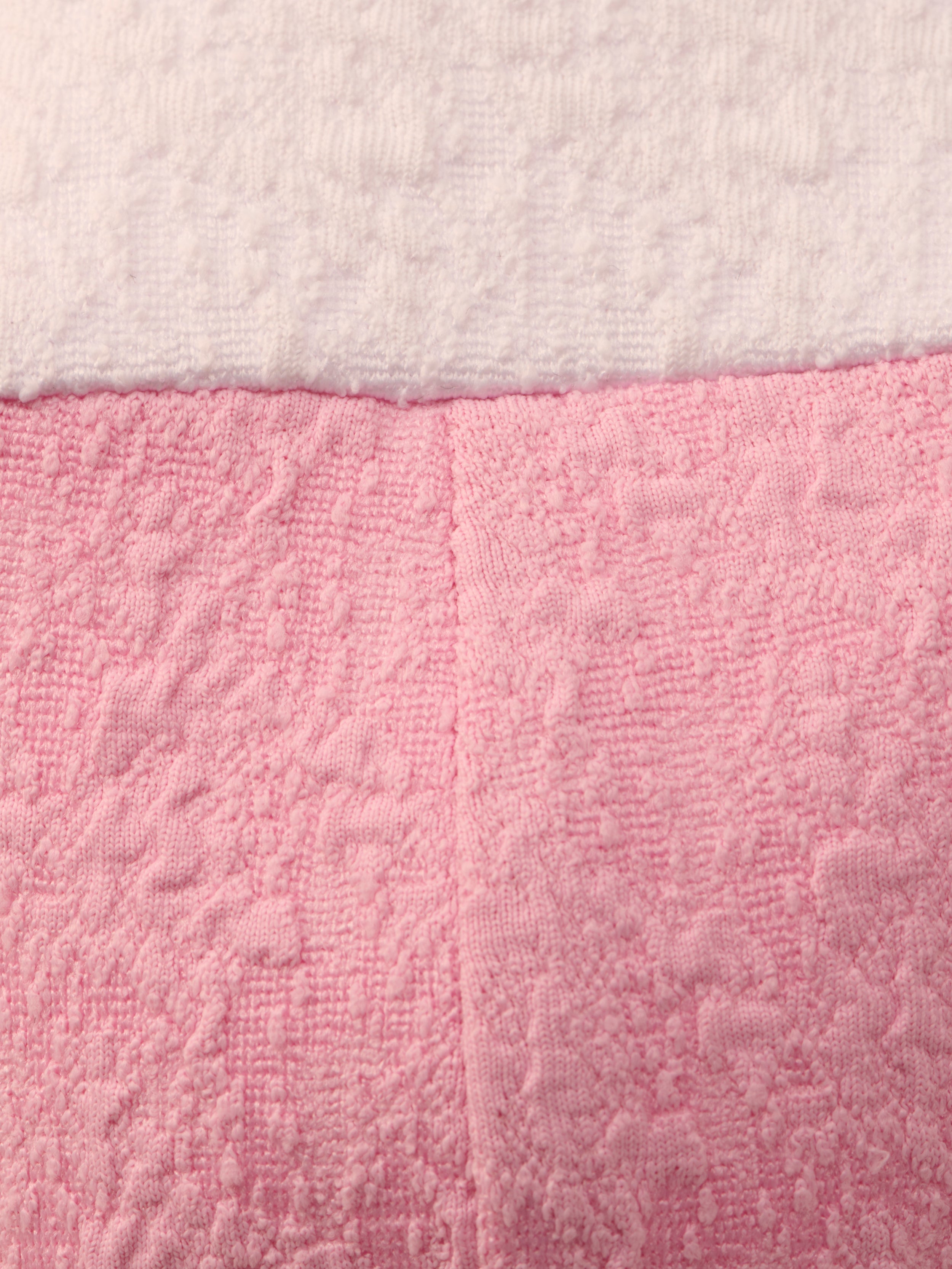 Close-up of the Alexandria Bikini Top’s textured bouclé fabric: white on top, pink on bottom, divided by a horizontal seam. The pink section is shaped like a balconette with underwire and has a vertical center seam.