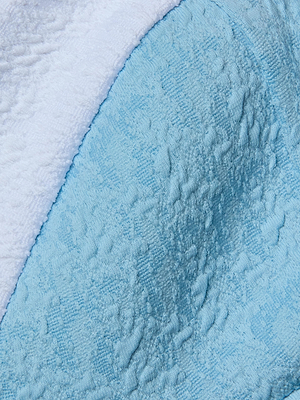 Close-up of bouclé swim fabric with a curved border; the top is white and the bottom is powder blue, both with a soft, towel-like look—ideal for the modern Alexandria Bikini Top.