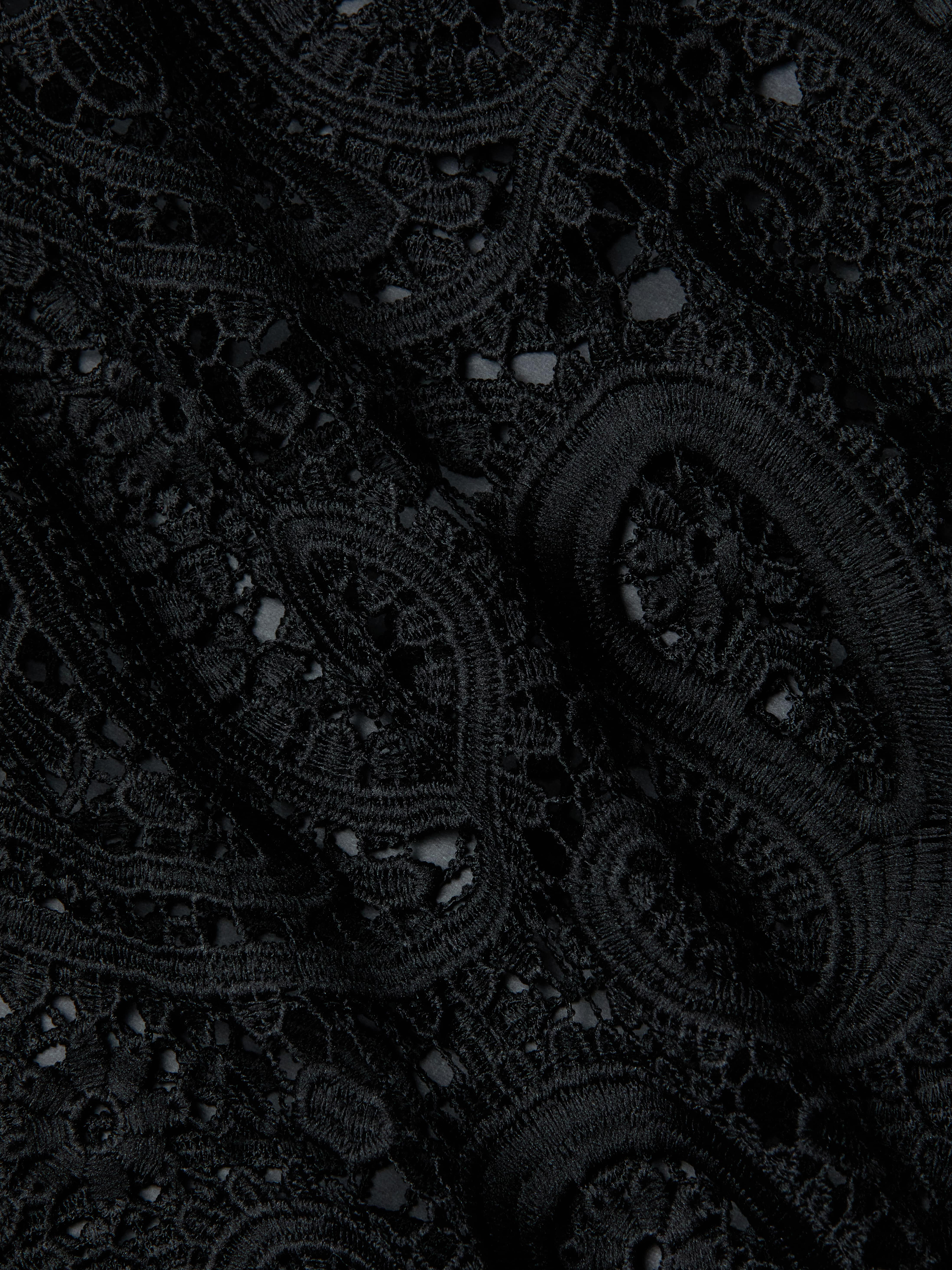 Close-up of the Ansley Cover-Up Dress, featuring intricate black lace fabric with swirling paisley and floral patterns, showcasing textured embroidery and delicate openwork details reminiscent of boho style.