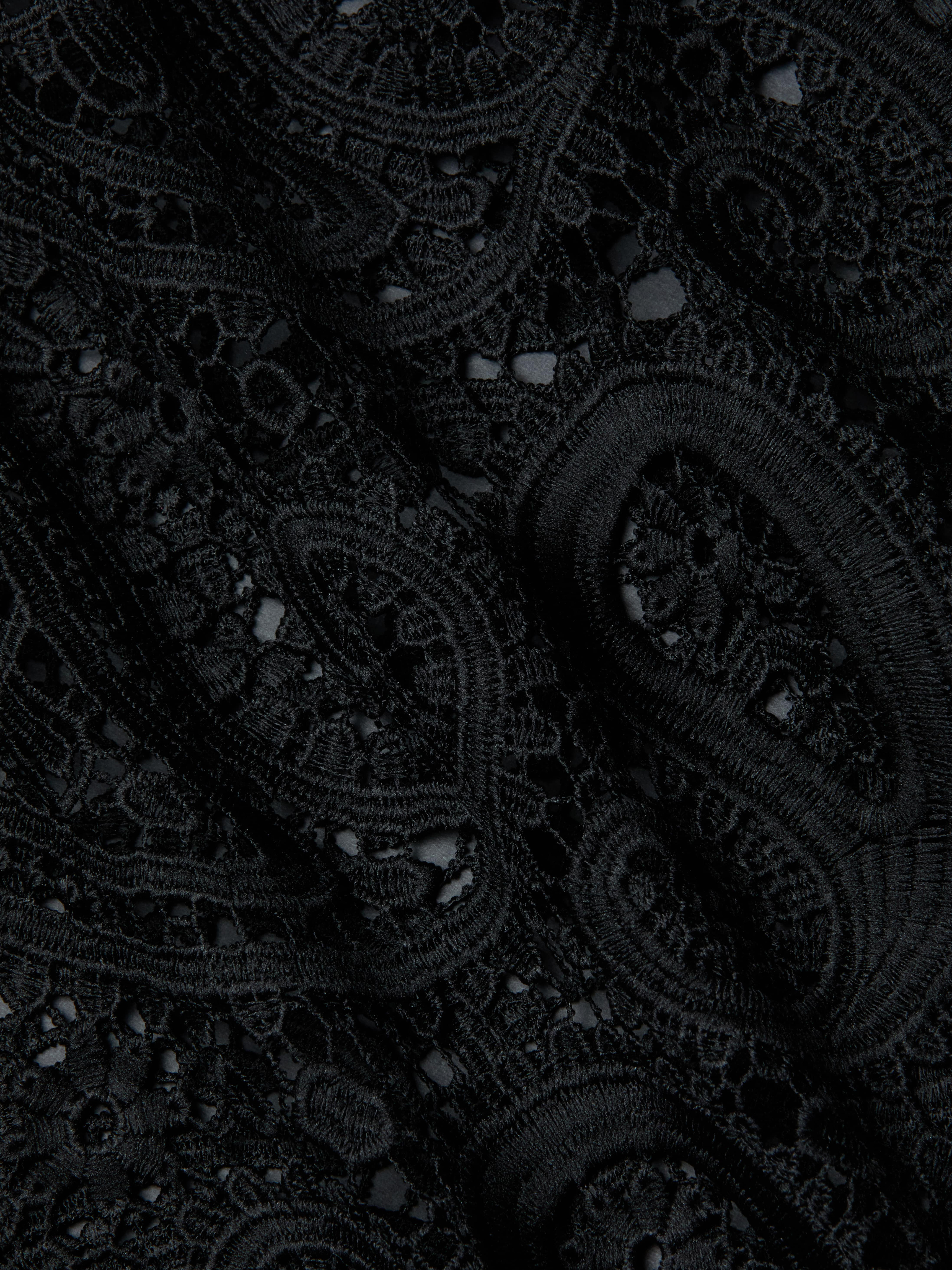 Close-up of the Ansley Cover-Up Dress, featuring intricate black lace fabric with swirling paisley and floral patterns, showcasing textured embroidery and delicate openwork details reminiscent of boho style.