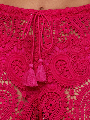 Close-up of the Geraldine Cover-Up Pant: a bright pink, sheer paisley lace pant featuring intricate floral crochet patterns, a drawstring waistband, and tassel details.