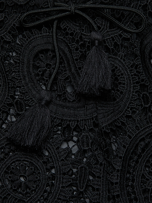 Close-up of the Geraldine Cover-Up Pant’s intricate black lace with paisley crochet-like circles and two black tassels on a cord, exuding resort wear elegance as it lays gracefully on the surface.