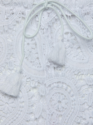 Close-up of the Geraldine Cover-Up Pant showcasing intricate white lace with floral and circular patterns, a drawstring tie, and tassel ends—perfect for adding bohemian flair to your resort wear.