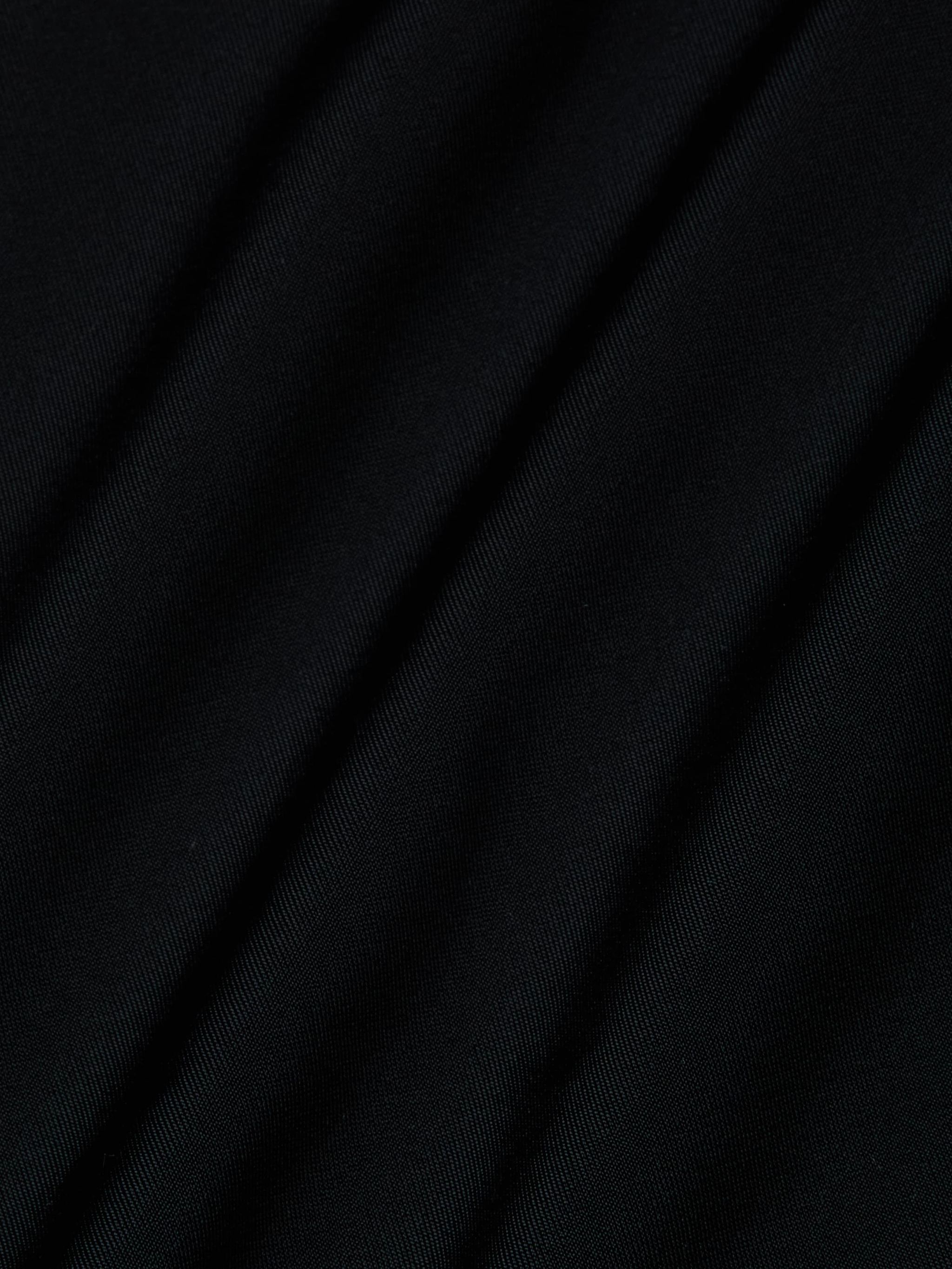 Close-up of the Violet String Bikini Bottom in black, featuring diagonal folds that reveal its smooth, slightly shiny texture and soft shadows between the creases.
