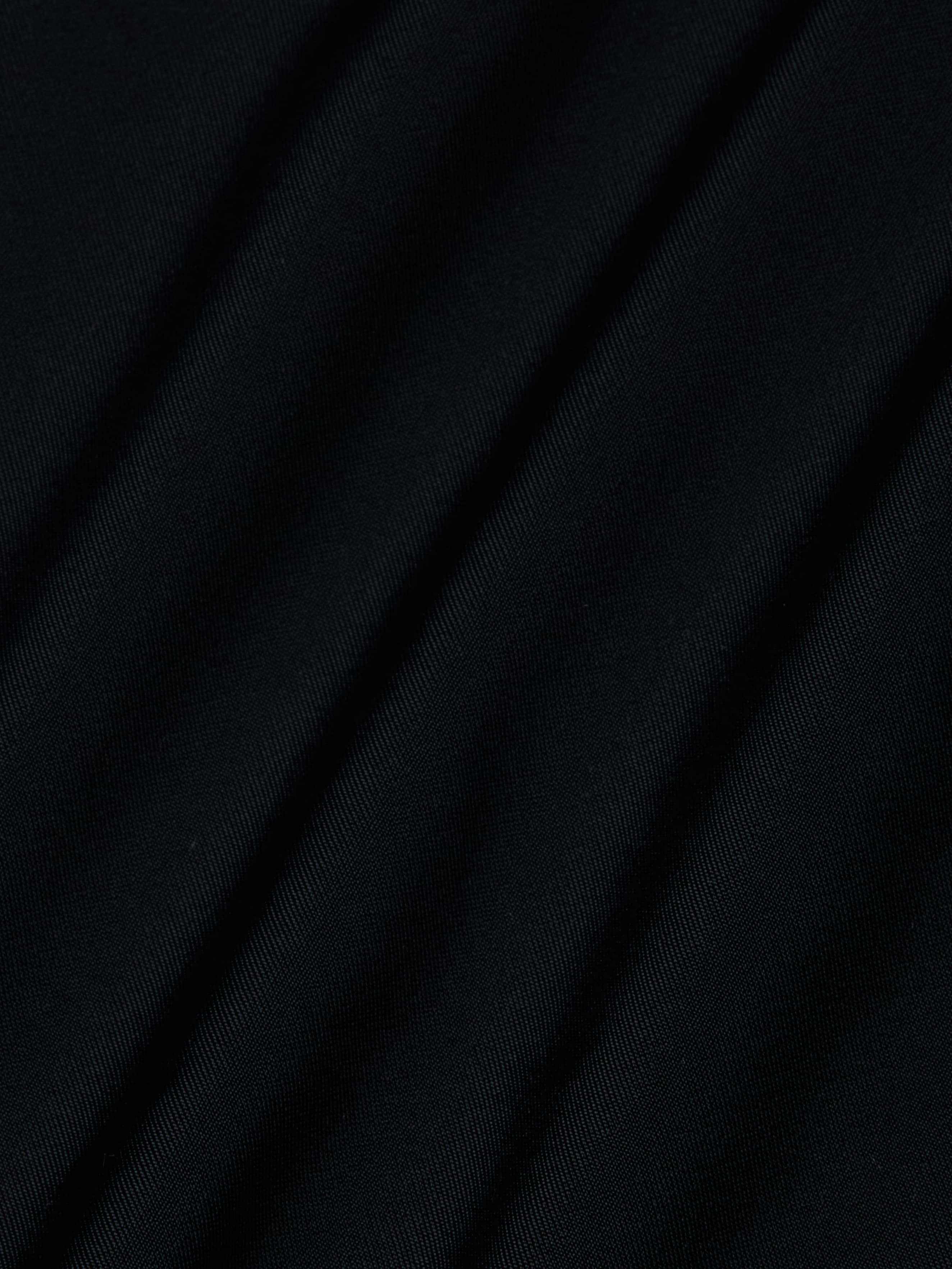 Close-up of black fabric from the Shiva One-Piece Swimsuit, featuring diagonal folds and a smooth, slightly shiny texture.