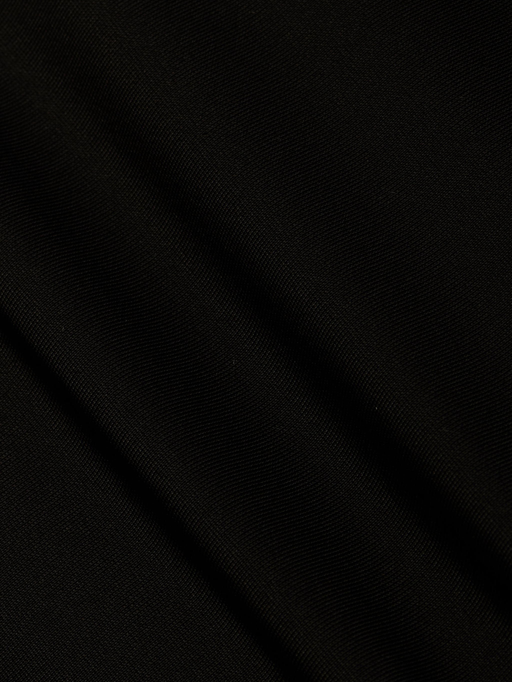 A close-up of black fabric from the Gabrielle One-Piece Swimsuit, featuring subtle diagonal folds and a fine, textured weave that evokes minimalist elegance.