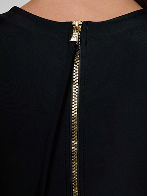 Close-up of the Lambert Paddlesuit by L'AGENCE—its black fabric features a striking gold zipper at the back, partially unzipped to reveal the upper back and neck, showcasing a sculpted silhouette with modern style.