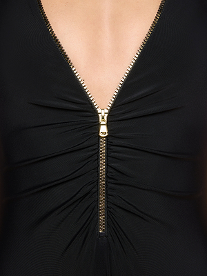Close-up of the Dorrie Plunge One-Piece Swimsuit in black, featuring a gold center zipper, UPF 50 protection, and vertical ruching along the front zip. Some skin is revealed at the neckline with the zipper partially unzipped.
