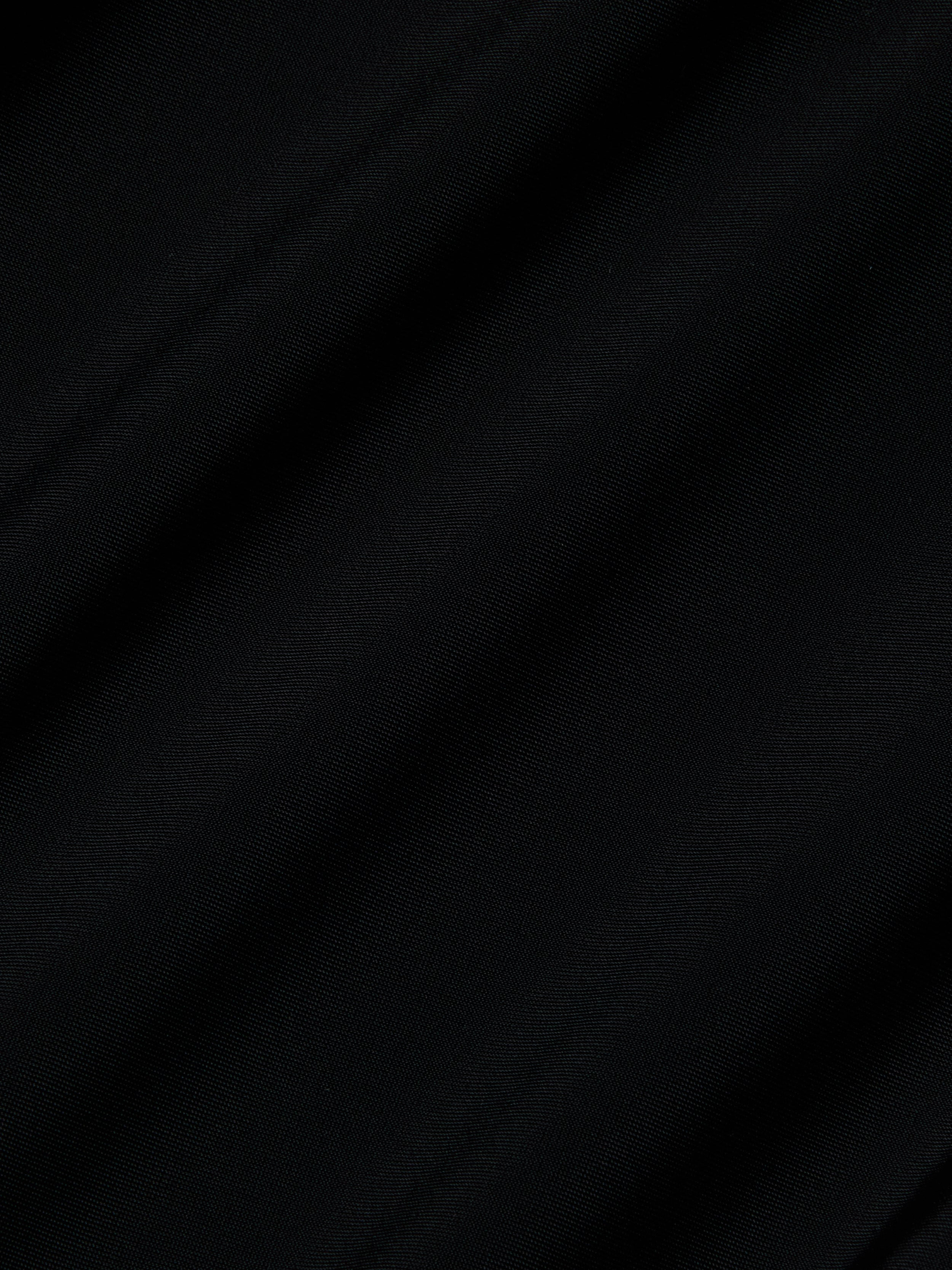 Close-up of the Akola One-Piece Swimsuit’s black UPF 50 fabric, featuring diagonal, subtle folds and a soft, lightly textured surface. The lighting casts gentle shadows that enhance the swimsuit’s smooth look.