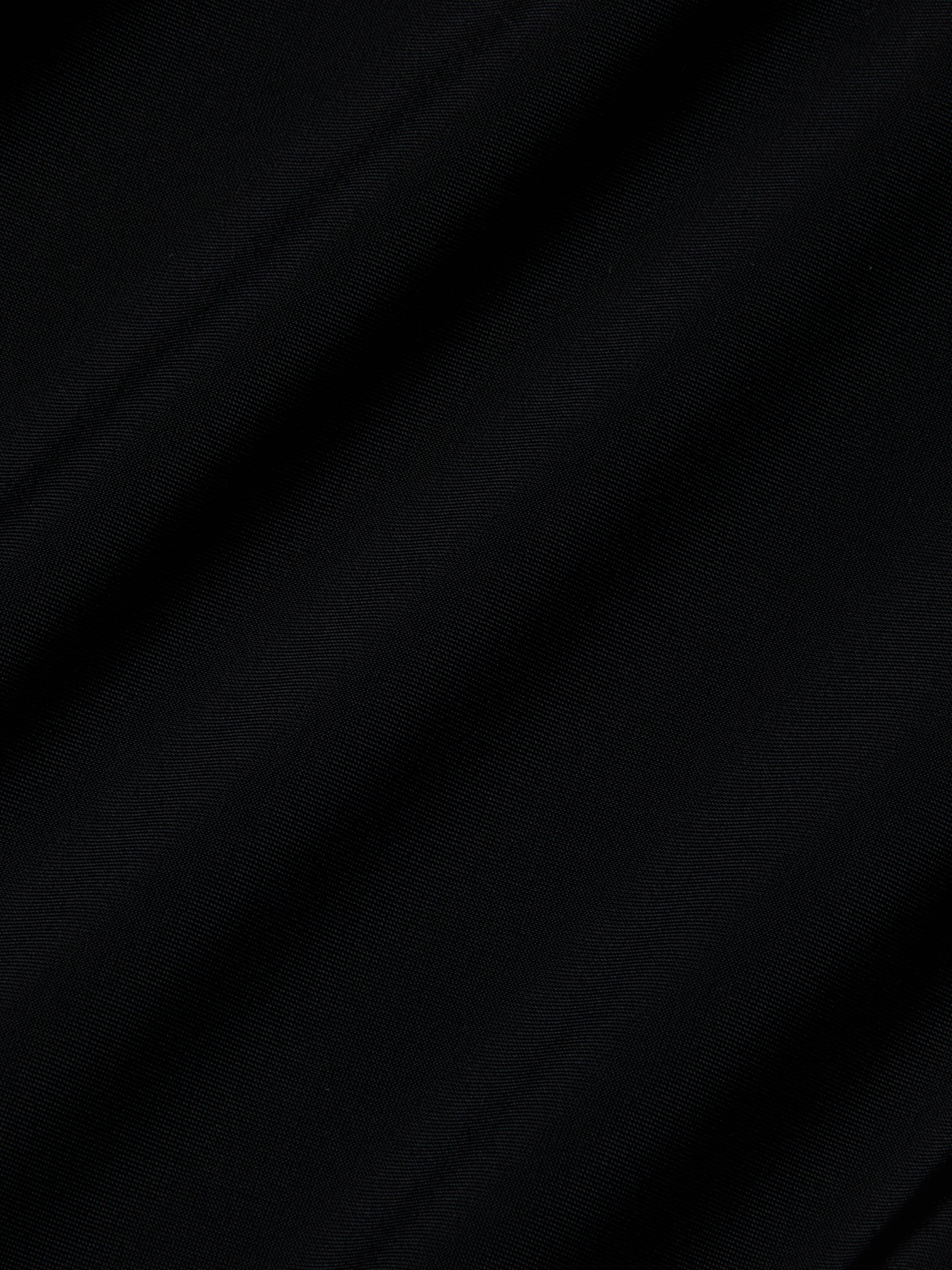 Close-up of the Akola One-Piece Swimsuit’s black UPF 50 fabric, featuring diagonal, subtle folds and a soft, lightly textured surface. The lighting casts gentle shadows that enhance the swimsuit’s smooth look.