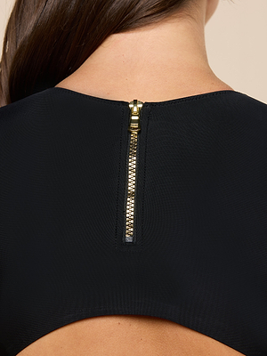 Close-up of a womans upper back in the Akola One-Piece Swimsuit, featuring a black open-back design with a gold zipper at the neckline. Her brown hair is partially visible.