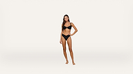 A woman stands barefoot against a plain white background, wearing a black bikini. She has long hair and one hand resting on her hip, looking confidently at the camera.