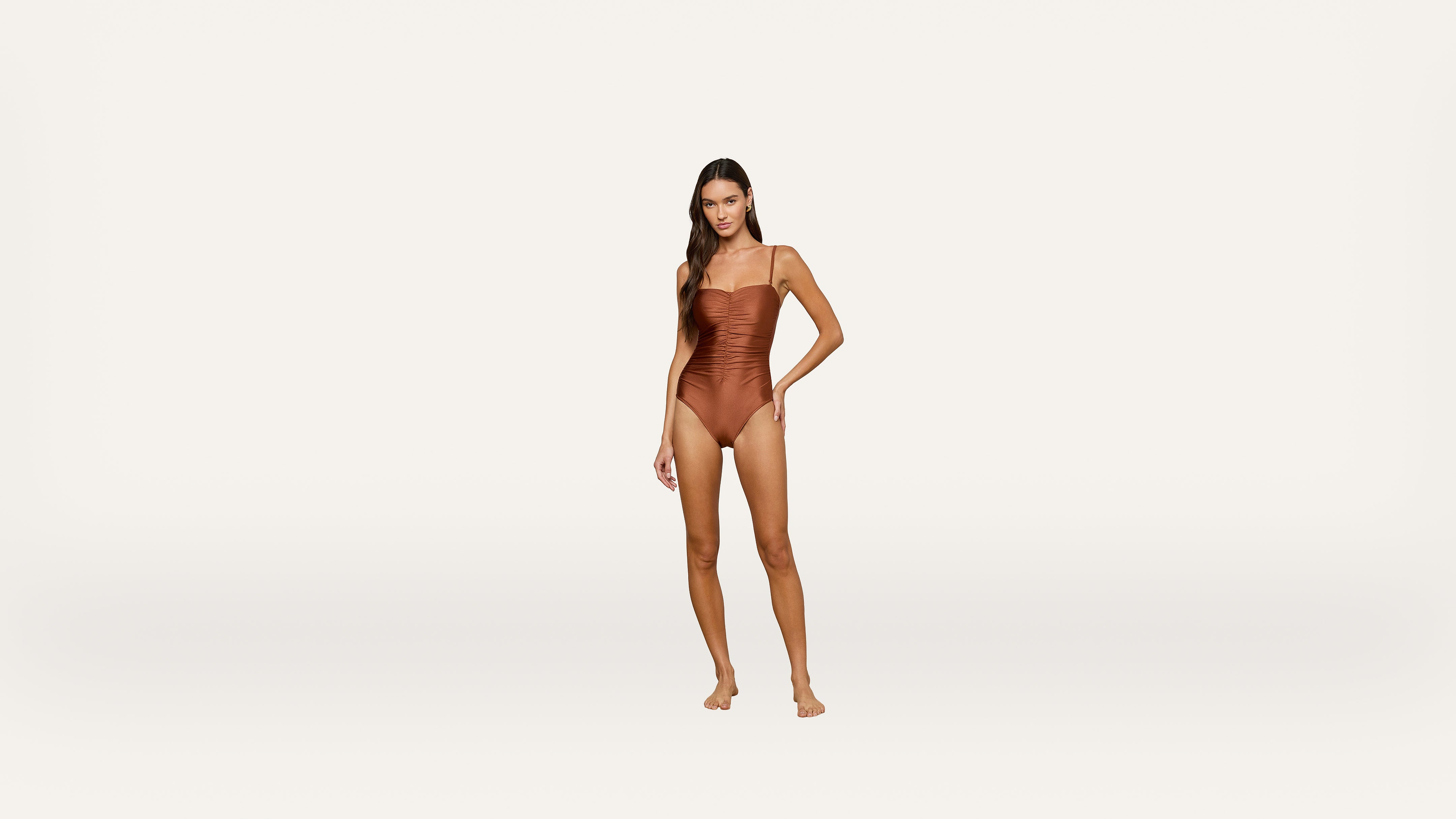 Woman standing barefoot, wearing a brown one-piece swimsuit, against a plain white background.