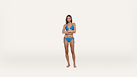 A woman wearing a blue bikini stands barefoot with her arms crossed against a plain white background.