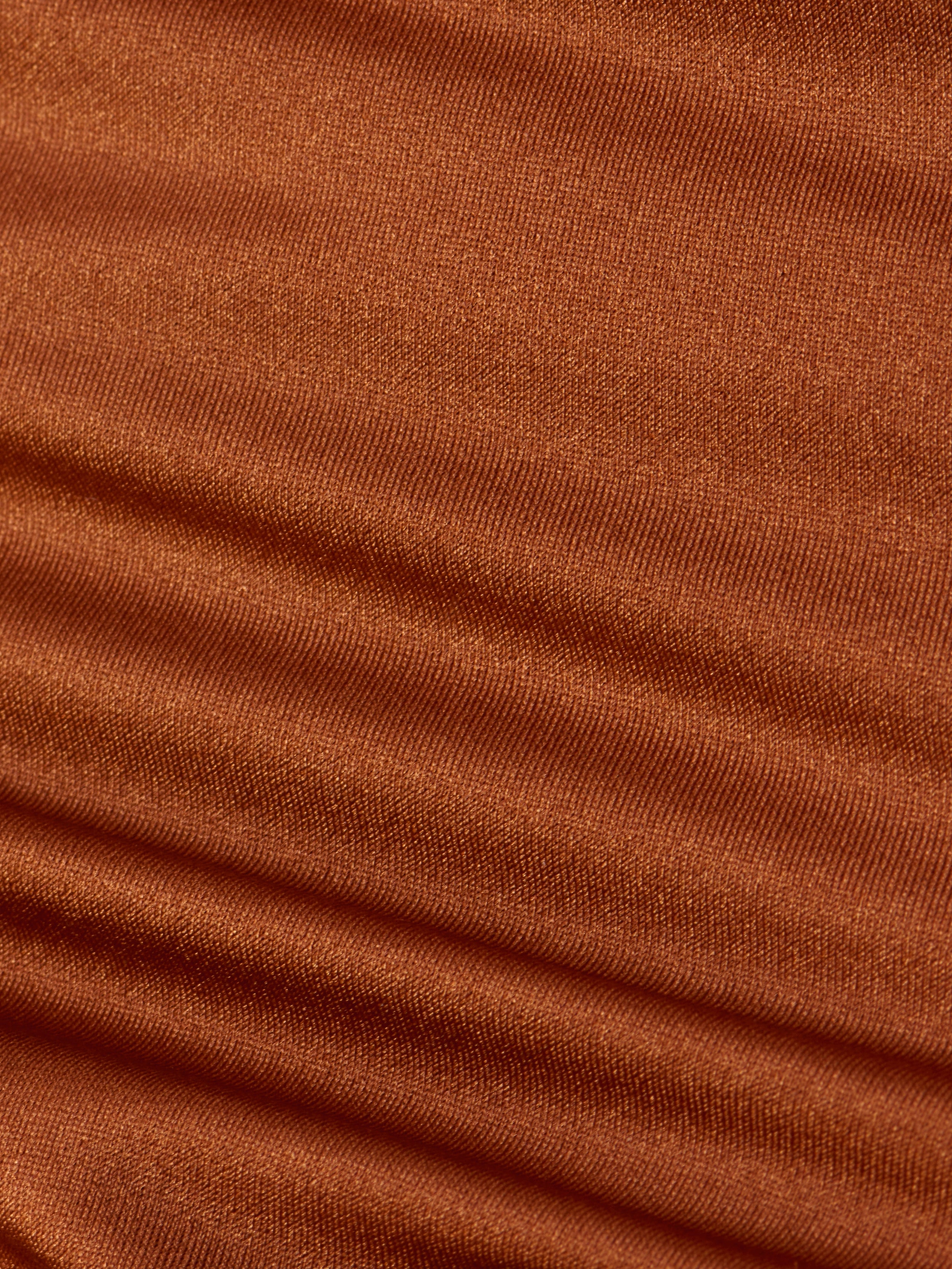 Close-up of rust-colored ribbed fabric displaying horizontal ridges and rich texture, softly lit to highlight the weave and folds—an ideal detail from the Britt Tie-Side Bikini Bottom, designed with adjustable tie sides and moderate coverage.