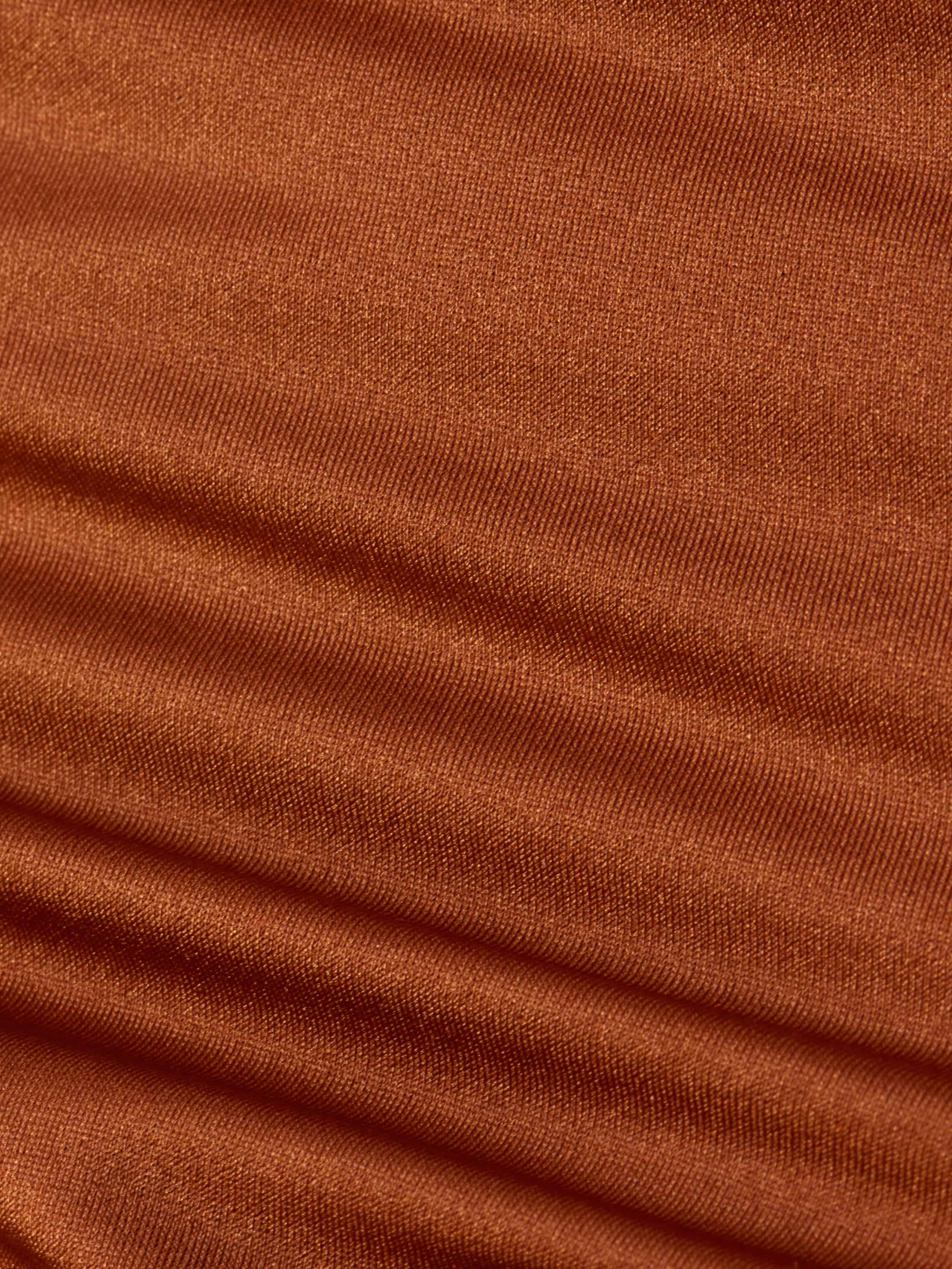 Close-up of rust-colored ribbed fabric displaying horizontal ridges and rich texture, softly lit to highlight the weave and folds—an ideal detail from the Britt Tie-Side Bikini Bottom, designed with adjustable tie sides and moderate coverage.