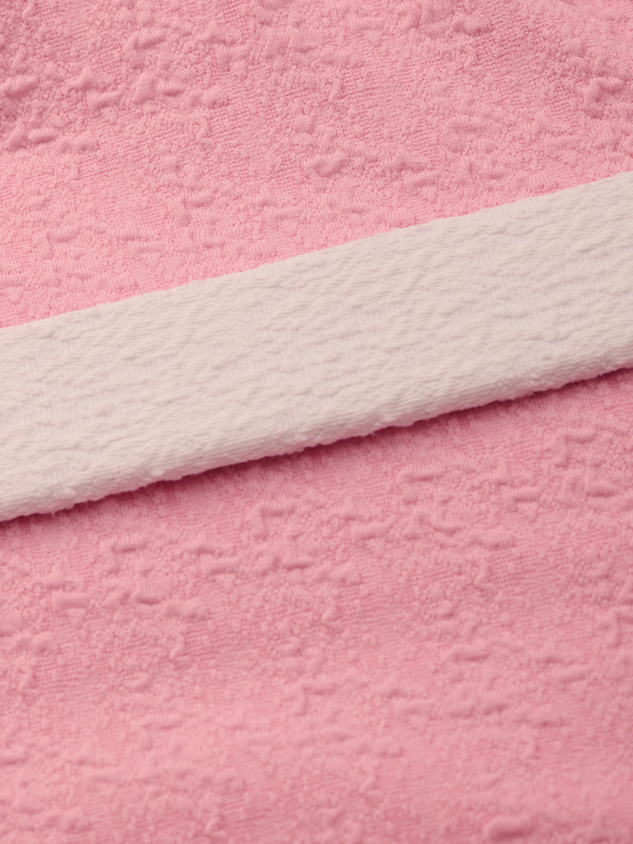 Close-up of soft pink bouclé nylon fabric with a subtle textured pattern and a white textured strip laid across it diagonally, similar to the luxurious materials used in the Amie Bandeau One-Piece Swimsuit.