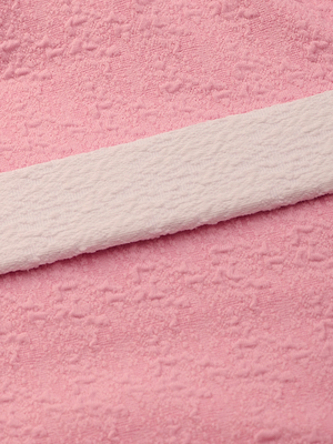 Close-up of soft pink bouclé nylon fabric with a subtle textured pattern and a white textured strip laid across it diagonally, similar to the luxurious materials used in the Amie Bandeau One-Piece Swimsuit.