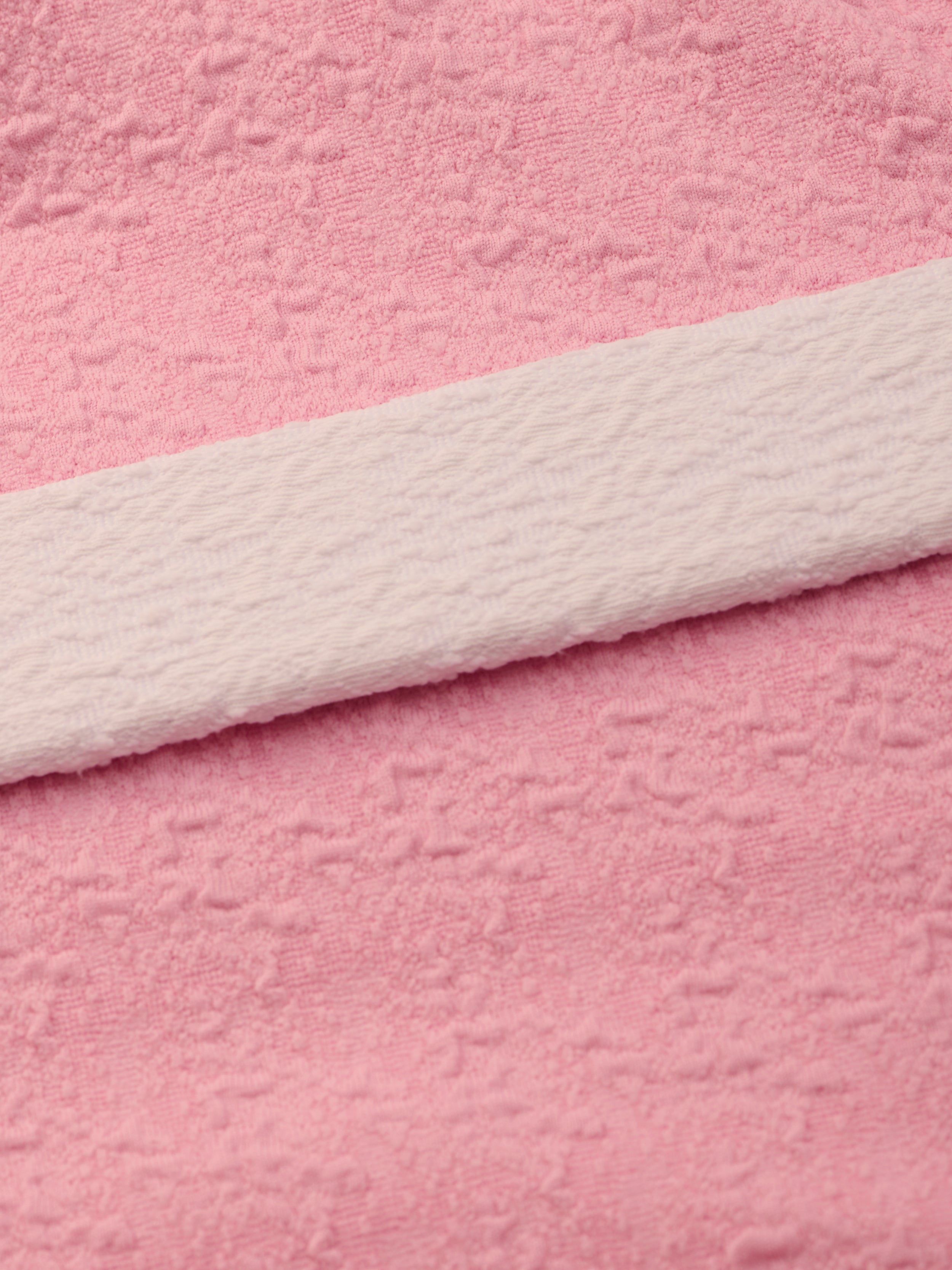 Close-up of soft pink bouclé nylon fabric with a subtle textured pattern and a white textured strip laid across it diagonally, similar to the luxurious materials used in the Amie Bandeau One-Piece Swimsuit.