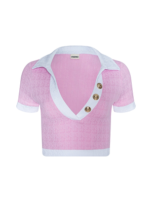 The Anastasia Cropped Rashguard is a light pink, short-sleeve textured polo swim top with water-safe bouclé fabric, a deep V-neckline and crisp white collar, finished with three decorative gold buttons.