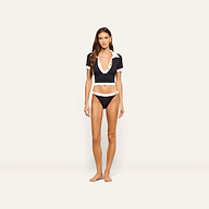A woman stands barefoot against a plain, light background wearing a deep V-neck black and white short-sleeve cropped top paired with the Jean Bikini Bottom—matching high-leg cut bikini bottoms crafted from textured bouclé fabric.