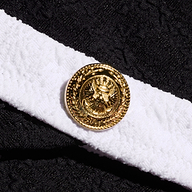 A gold button with an embossed eagle emblem is attached to a textured bouclé white band on the Jean Bikini Bottom, set against a background of black fabric.