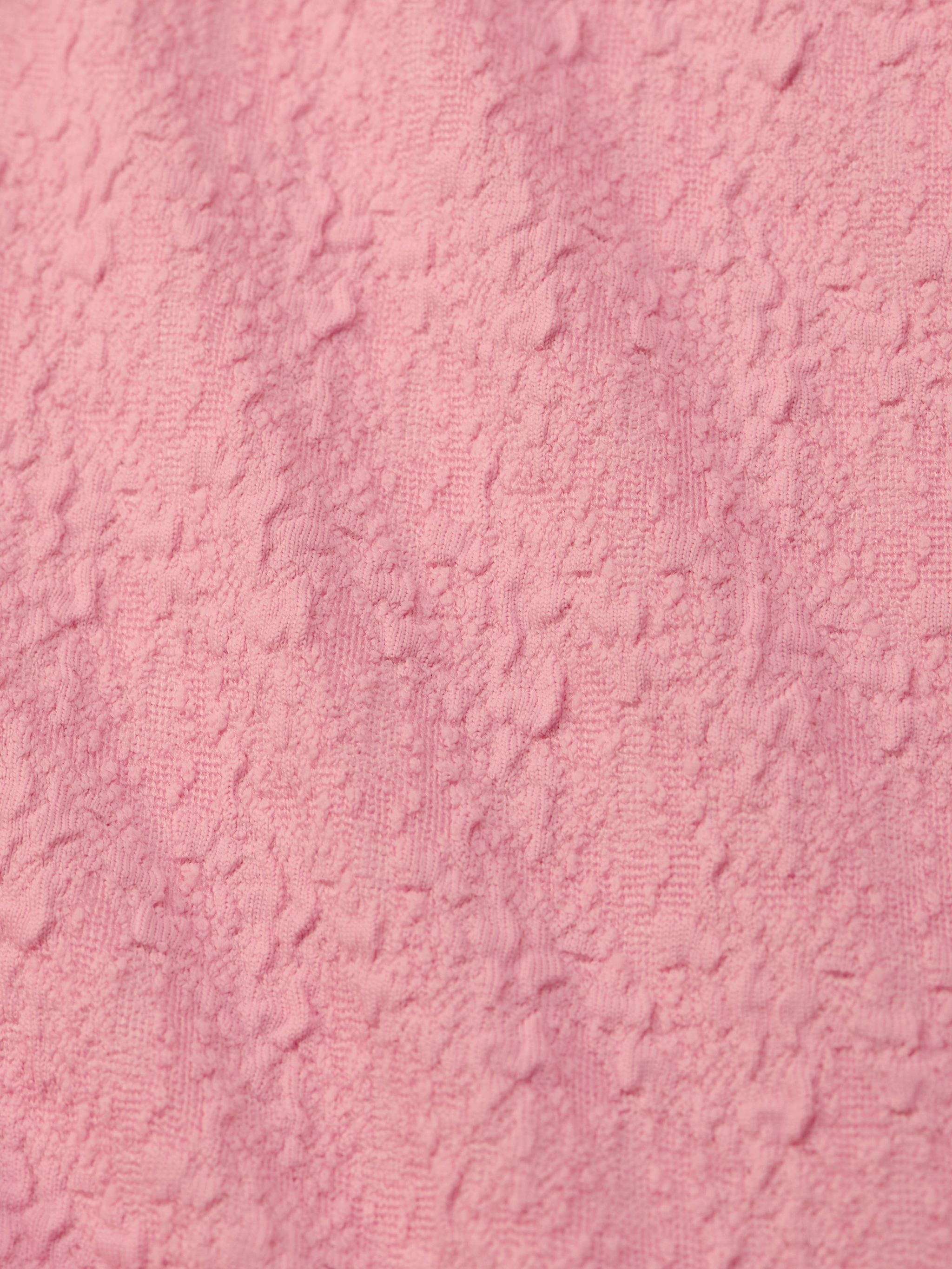 Close-up of the Jean Bikini Bottom’s textured pink bouclé fabric, featuring a soft, uneven surface with raised patterns—perfect for a chic high-leg cut and on-trend poolside style.