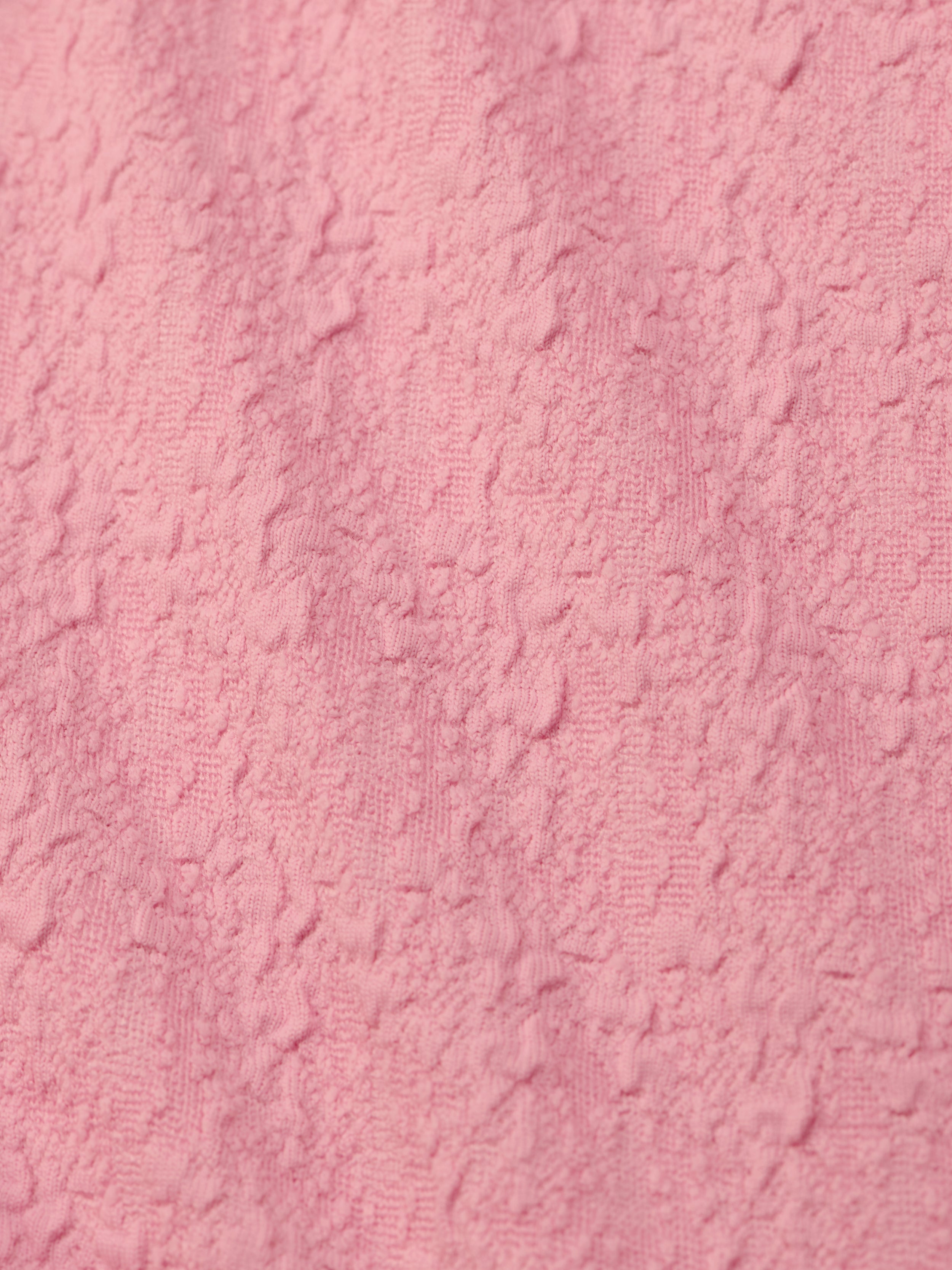 Close-up of the Jean Bikini Bottom’s textured pink bouclé fabric, featuring a soft, uneven surface with raised patterns—perfect for a chic high-leg cut and on-trend poolside style.