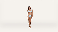 A woman wearing a light blue bikini stands barefoot against a plain white background, facing forward with a neutral expression.