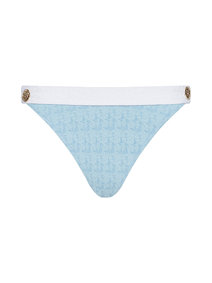 The Jean Bikini Bottom features light blue bouclé swim fabric with a subtle pattern, a white waistband, and gold decorative side buttons. Its sleek and minimalistic design offers a modern, stylish look.