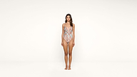 A woman stands barefoot against a plain white background, wearing a colorful patterned one-piece swimsuit. She faces forward with her arms relaxed at her sides.
