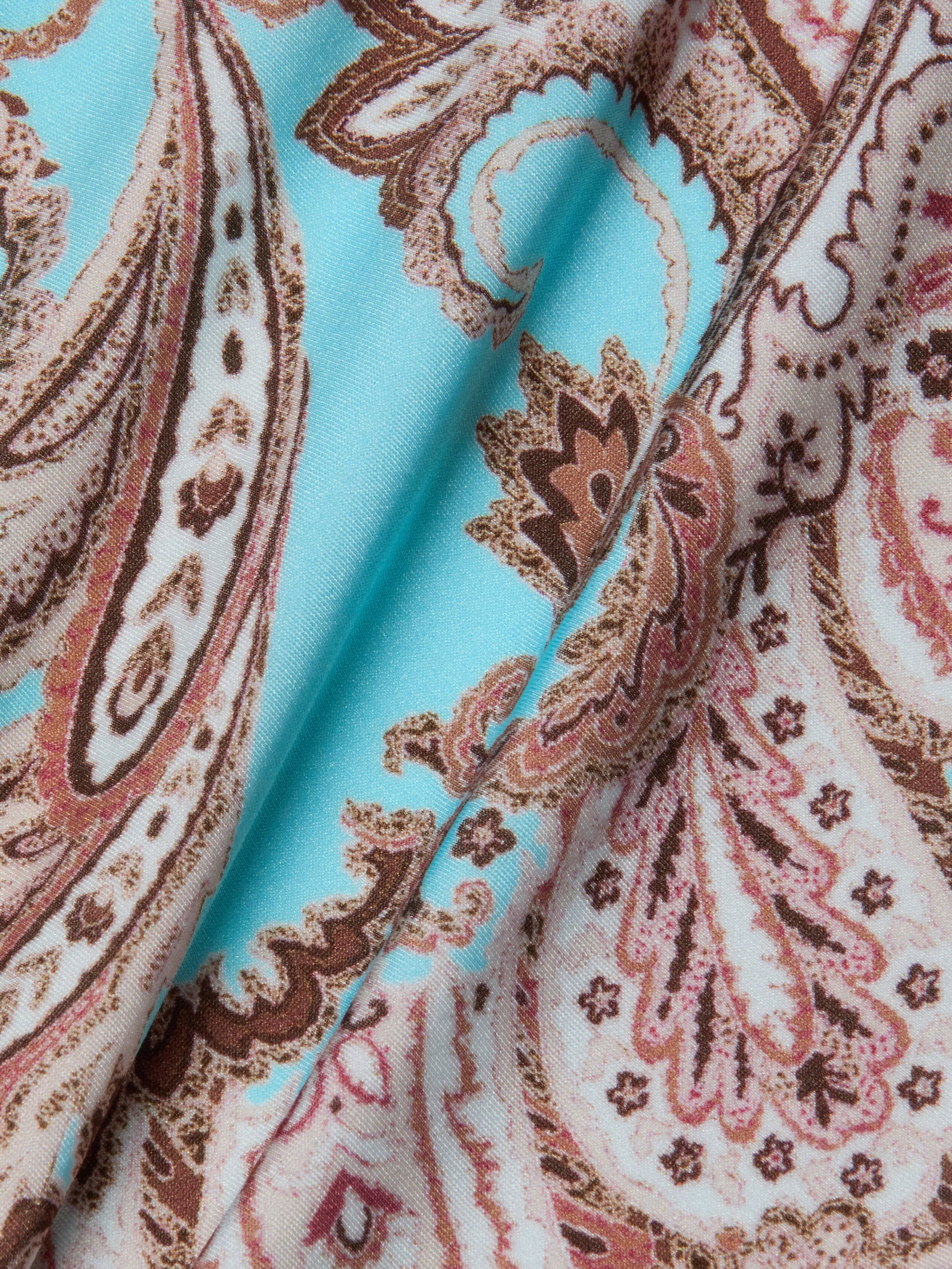 Close-up of the Remi One-Piece Swimsuit fabric, featuring a paisley print in shades of brown and beige on a light blue background. The slightly folded material highlights its texture and intricate, swirling designs—making it perfect for those who value both style and comfort in an elegant swimsuit.