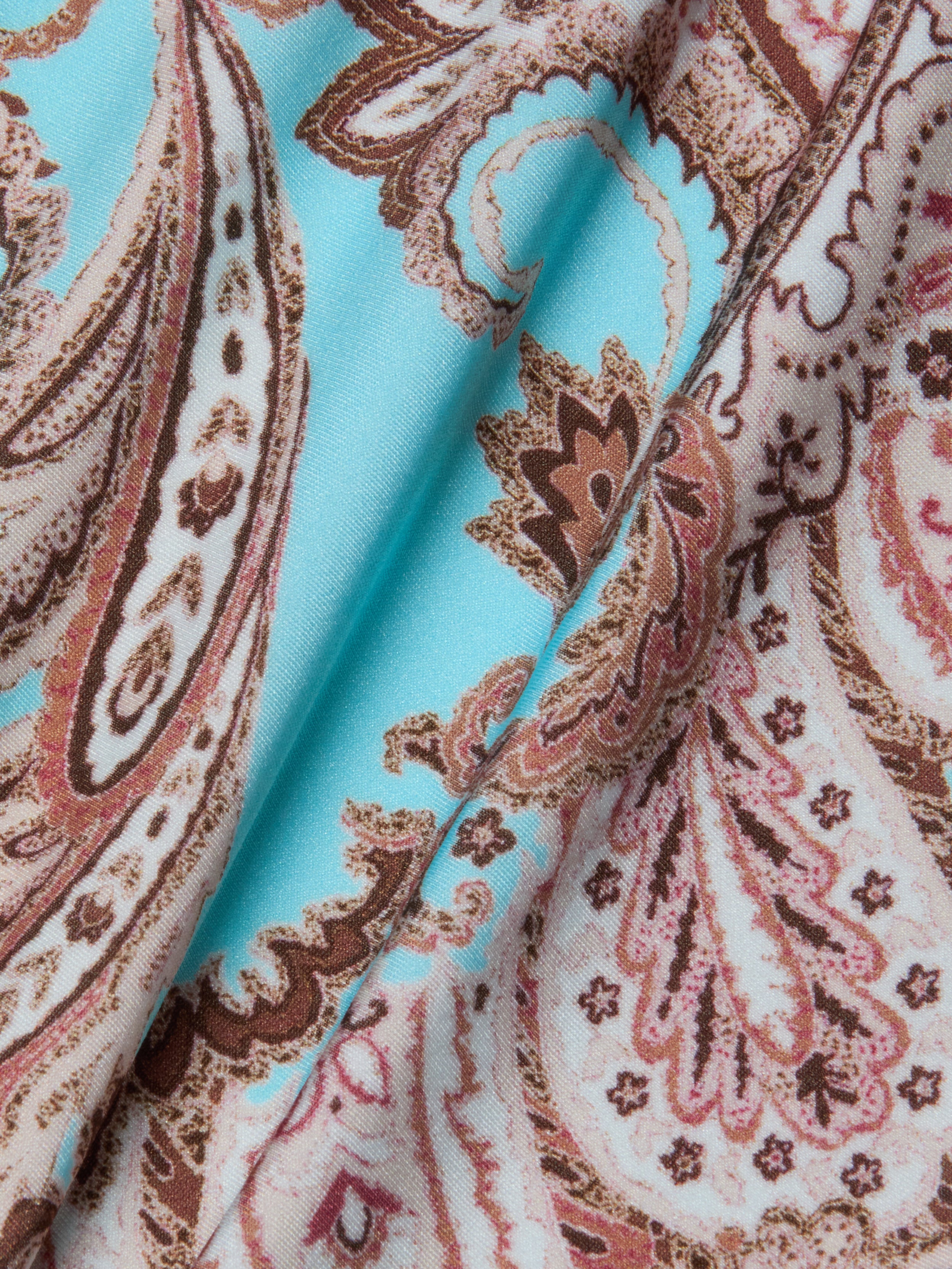 Close-up of the Remi One-Piece Swimsuit fabric, featuring a paisley print in shades of brown and beige on a light blue background. The slightly folded material highlights its texture and intricate, swirling designs—making it perfect for those who value both style and comfort in an elegant swimsuit.