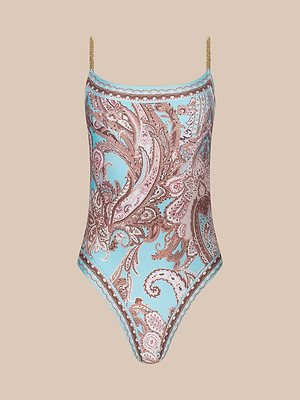 The Remi One-Piece Swimsuit features thin chain straps and a pink and brown paisley print on a light blue background, shown against a beige backdrop.